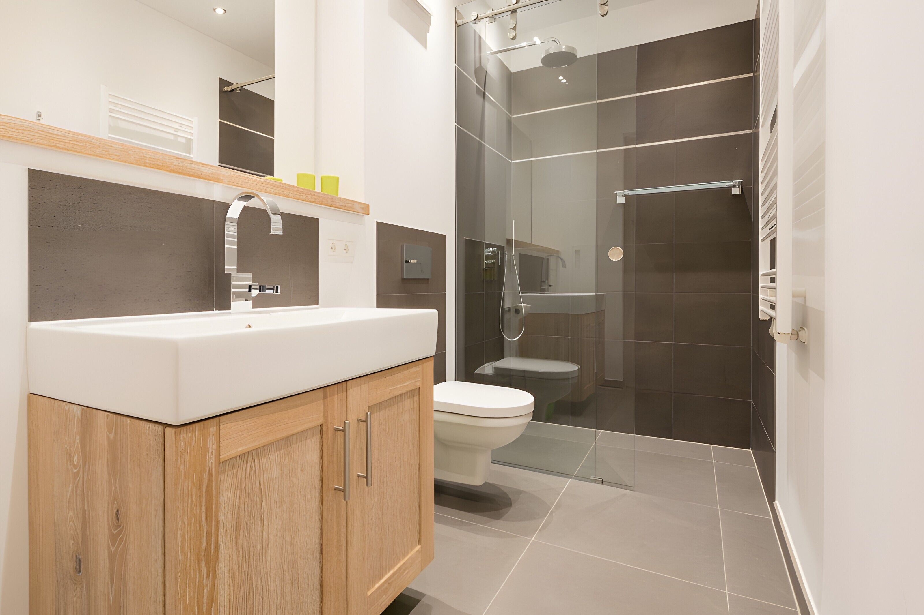 Et moderne badeværelse med en trækommode, toilet og et bruseområde med glasvægge.