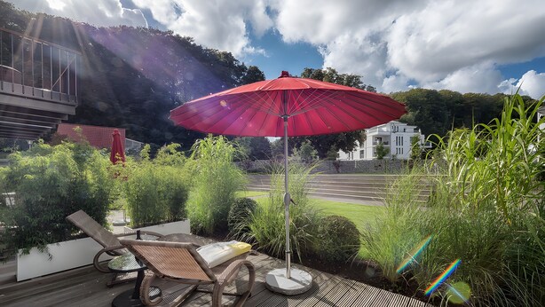 Un parapluie rouge, un fauteuil de jardin et une vue sur une route et des bâtiments.