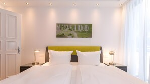 Une chambre d’hôtel comprenant un lit, deux tables de chevet, une petite table, un tableau accroché au mur et une porte.