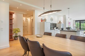 A modern kitchen with a dining area, featuring a wooden table and chairs, a pendant light, and a view of the outdoors.
