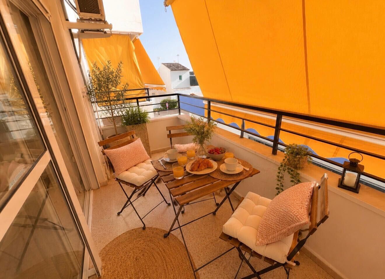 Un balcon avec une table préparée pour le petit-déjeuner, deux fauteuils confortables et une vue sur le paysage urbain.