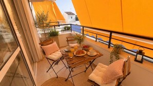 Ein Balkon mit einem Frühstückstisch, zwei gepolsterten Stühlen und Blick auf die Stadt.