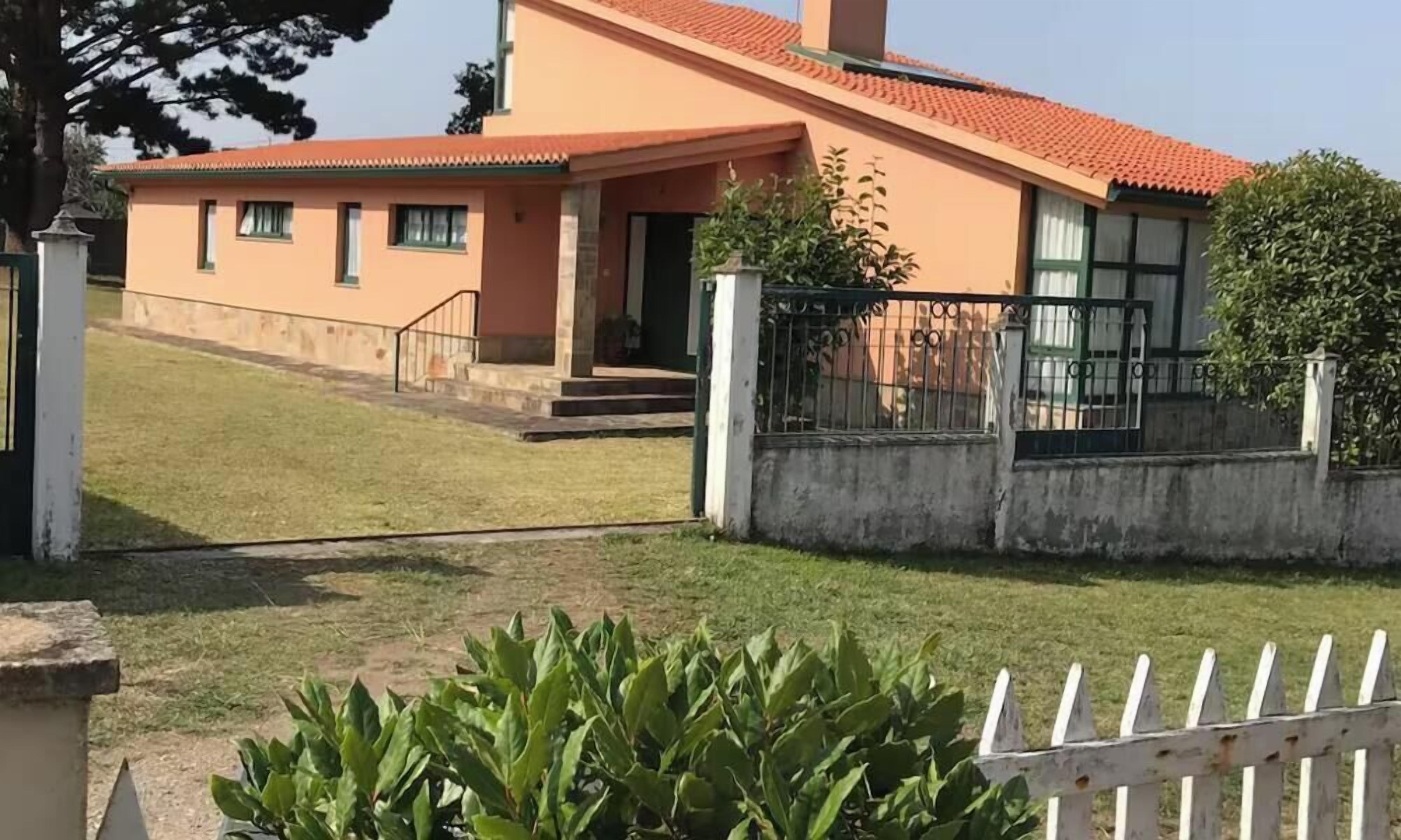 Um edifício de dois andares com telhado de telhas vermelhas, entrada frontal com degraus e cerca branca de piquete.