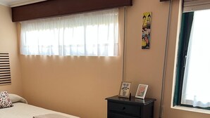 Ein Schlafzimmer mit Bett, Kommode, Heizkörper und einem Fenster mit Vorhängen.
