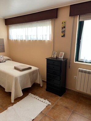 Een slaapkamer met een bed, een dressoir, een radiator en een raam met gordijnen.