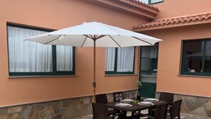 Eine Terrasse im Freien mit Steinboden, einem Tisch und Stühlen sowie einem weißen Sonnenschirm.