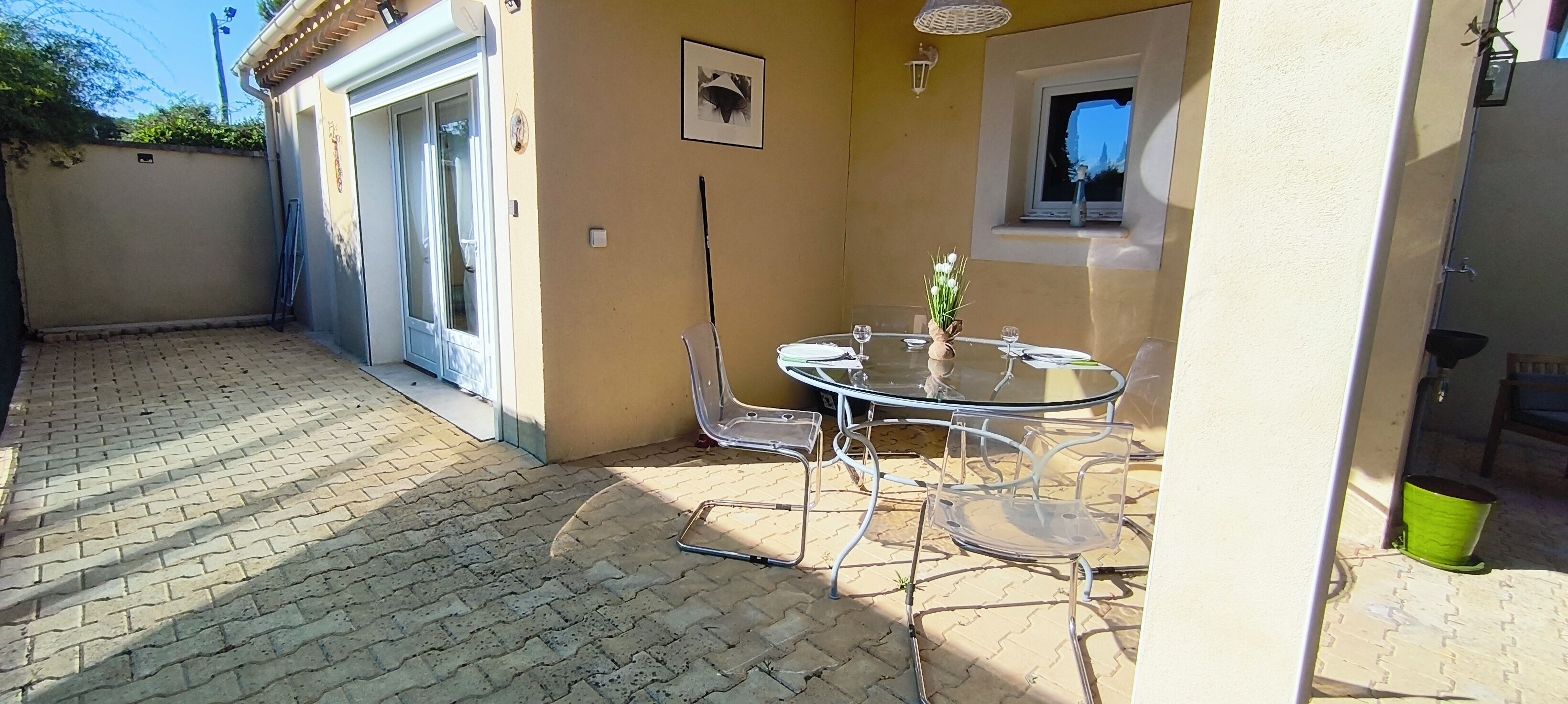 A patio with a round glass table and chairs, a small window, and a door leading to the interior.