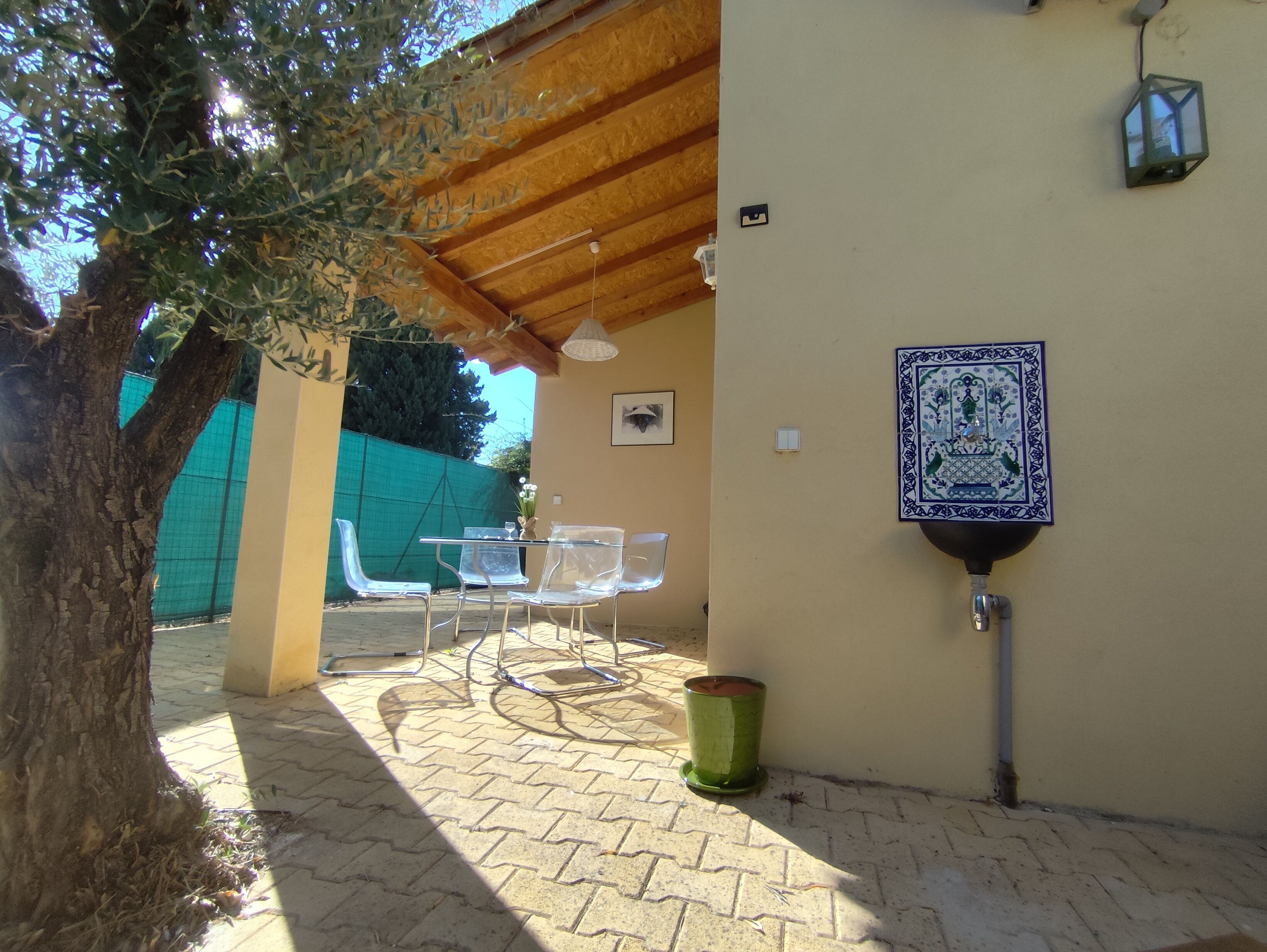 An outdoor patio with a table and chairs, a green trash bin, and a decorative wall piece.