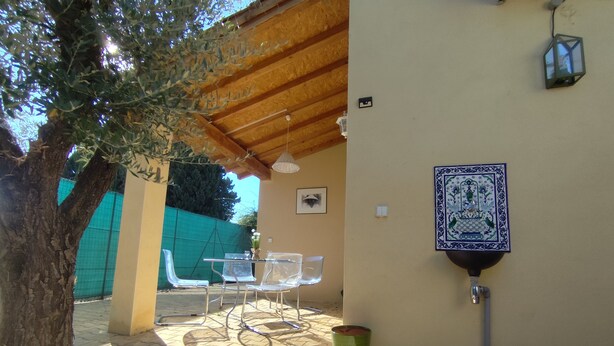 Un patio al aire libre con una mesa y sillas, un basurero verde y un adorno en la pared.