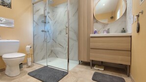 Un baño con ducha de vidrio, inodoro, lavamanos con espejo y un perchero para toallas.