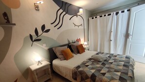 Un dormitorio con una cama, mesitas de noche, un mural en la pared y una puerta con cortinas.