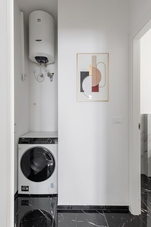 A laundry room with a front-loading washer and dryer, a water heater, and a wall-mounted artwork. - La Corte Vermena by Wonderful Italy (Bologna)