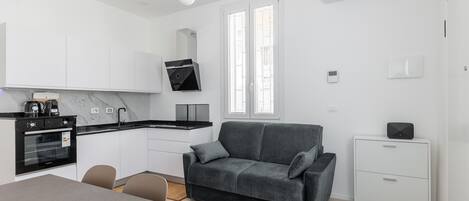 Una cocina moderna con horno empotrado, una mesa de comedor con sillas, un sofá gris y un pequeño armario blanco.