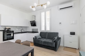 A modern kitchen with a built-in oven, a dining table with chairs, a grey sofa, and a small white cabinet. - La Corte Vermena by Wonderful Italy (Bologna)