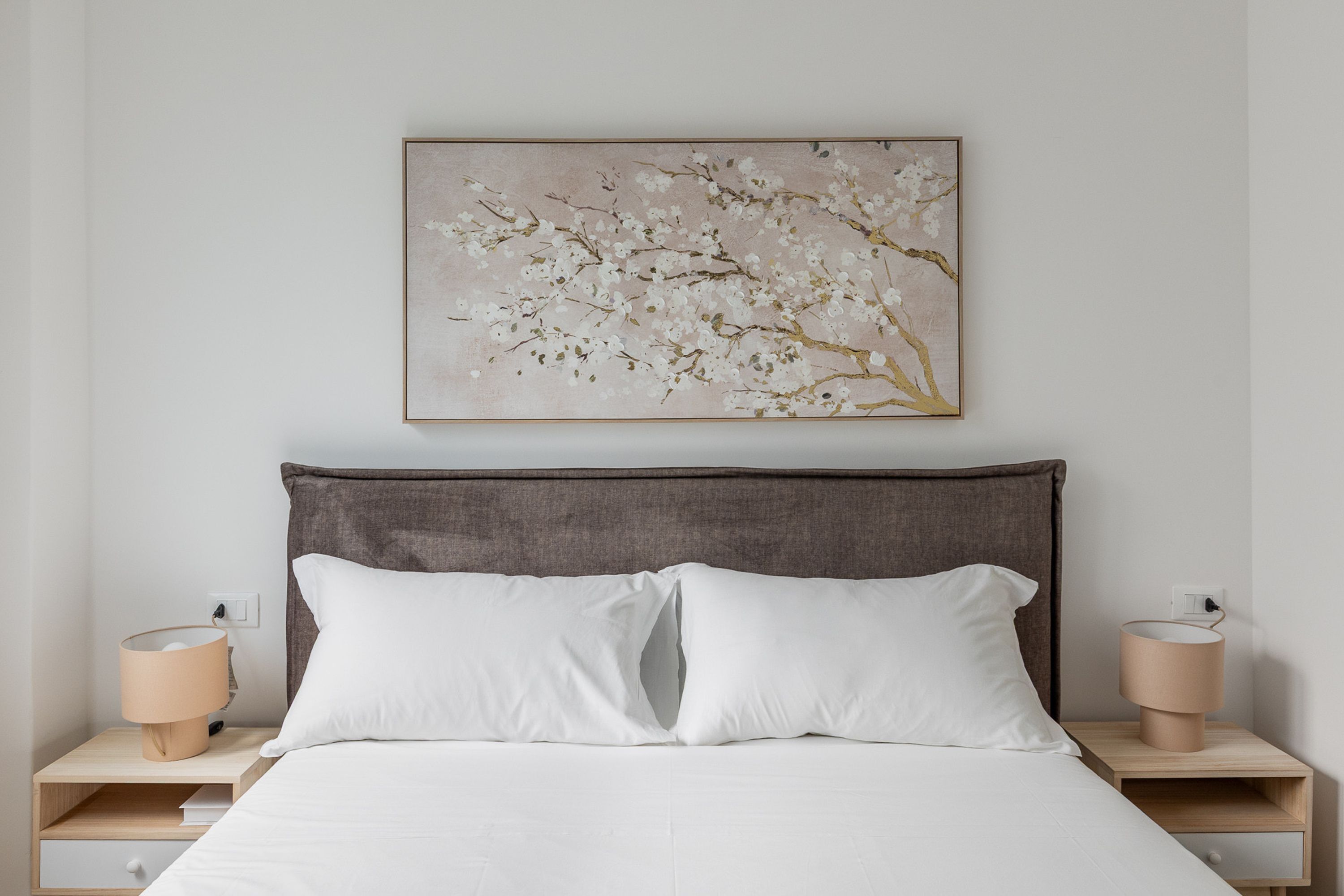 A bedroom with a bed, two bedside tables, and a wall-mounted artwork of a flower branch.