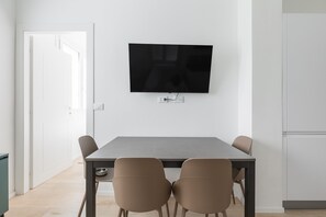 A modern dining area with a flat-screen TV mounted on the wall, a grey table, and four chairs. - La Corte Vermena by Wonderful Italy (Bologna)