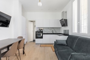 A modern kitchen with a built-in oven, a dining area with a table and chairs, and a grey sofa. - La Corte Vermena by Wonderful Italy (Bologna)