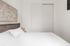 Een slaapkamer met een bed, nachtkastje, lamp en een kledingkast.