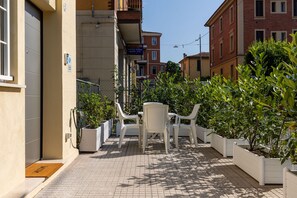 A narrow outdoor corridor with a row of white plastic chairs and tables, surrounded by potted plants. - La Corte Vermena by Wonderful Italy (Bologna)