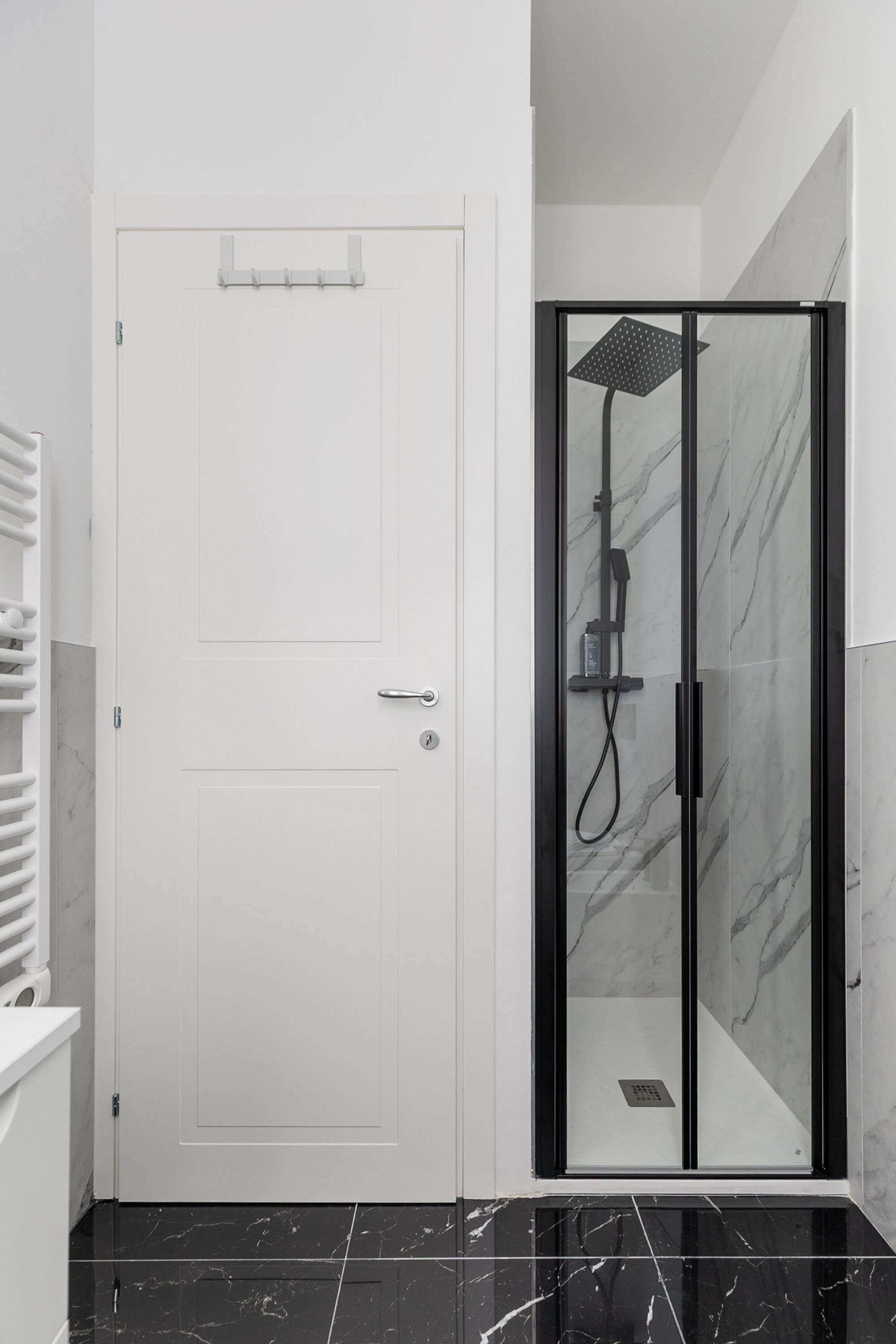 Un bagno moderno con una porta bianca, una cabina doccia in vetro e pavimenti in marmo.