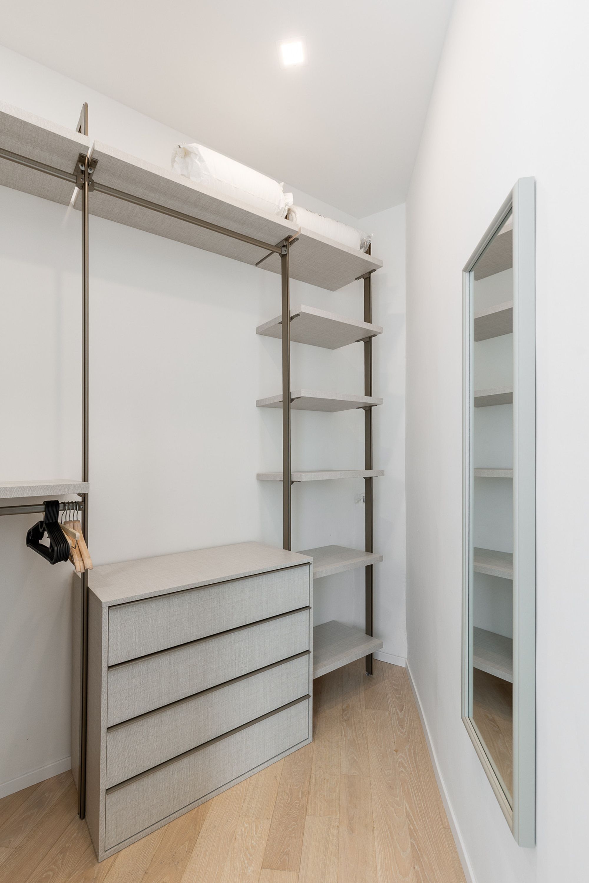 A walk-in closet with a built-in bench, multiple shelves, and a mirrored closet door.
