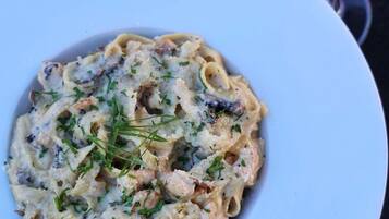A plate of pasta with a creamy sauce, garnished with herbs, and a glass of orange juice on the side.