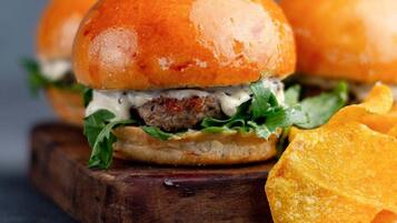 A burger with lettuce and a sauce, placed on a wooden board.