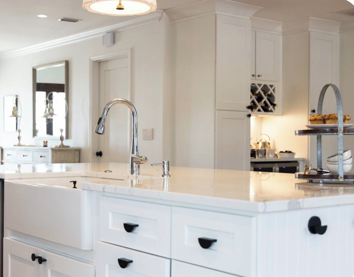 A modern kitchen with white cabinetry, a central island with a sink, and a hanging light fixture.