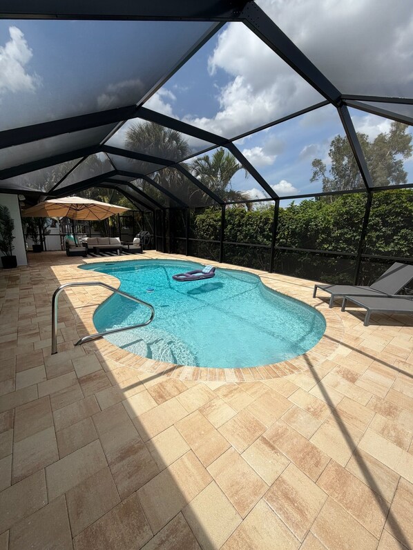 An outdoor swimming pool with a glass ceiling, surrounded by lounge chairs and a sunbed.