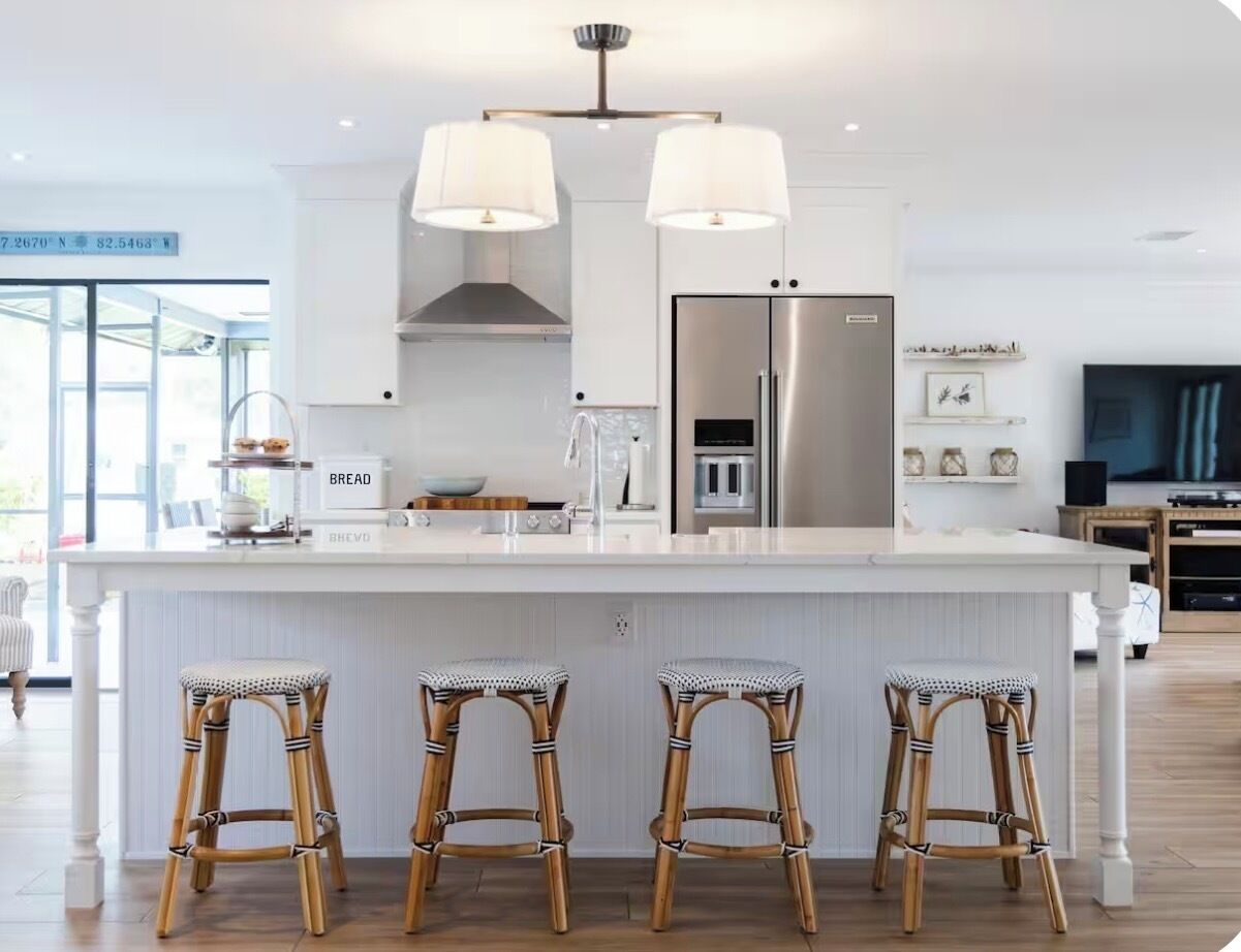 Une cuisine moderne dotée d’un îlot central, de tabourets de bar, d’un réfrigérateur en acier inoxydable et de luminaires suspendus.