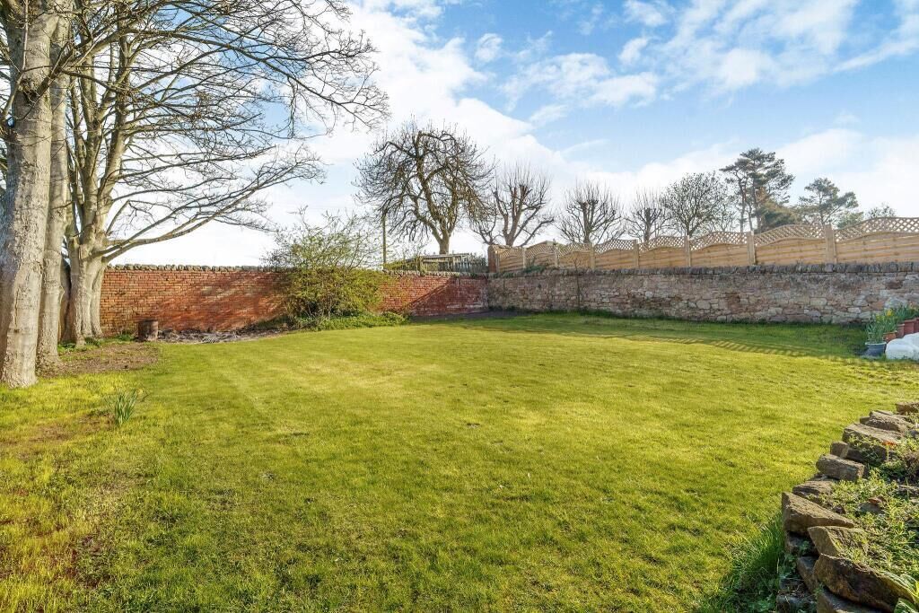 A well-maintained grassy backyard with a stone wall, trees, and a wooden fence.