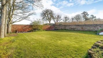 A well-maintained grassy backyard with a stone wall, trees, and a wooden fence.