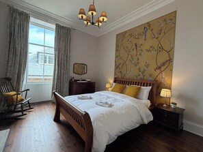 A hotel room with a wooden bed, a nightstand with a lamp, a chair, a window with curtains, and a wall with a bird mural. - Peaceful 6-bedroom house for family and group in charming Berwick-upon-Tweed (Berwick-upon-Tweed)