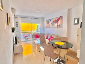 A modern living room with a glass dining table, a sofa set, and a large abstract painting on the wall. - Terrasol Keops Caleta de Velez (Velez-Malaga)