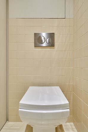 Une salle de bain avec des toilettes blanches, des murs recouverts de carreaux beiges et un panneau de commande pour la chasse d’eau.