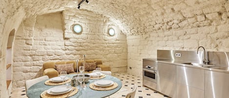 Comedor con una mesa redonda dispuesta para cuatro personas, un sofá y una cocina con un lavaplatos de acero inoxidable y un horno.