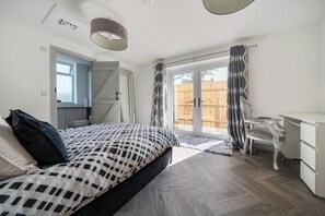 Un dormitorio con cama, un escritorio y una silla. Hay una ventana y una puerta.