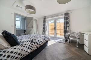 Quarto com cama, escrivaninha e cadeira. Há uma janela e uma porta.