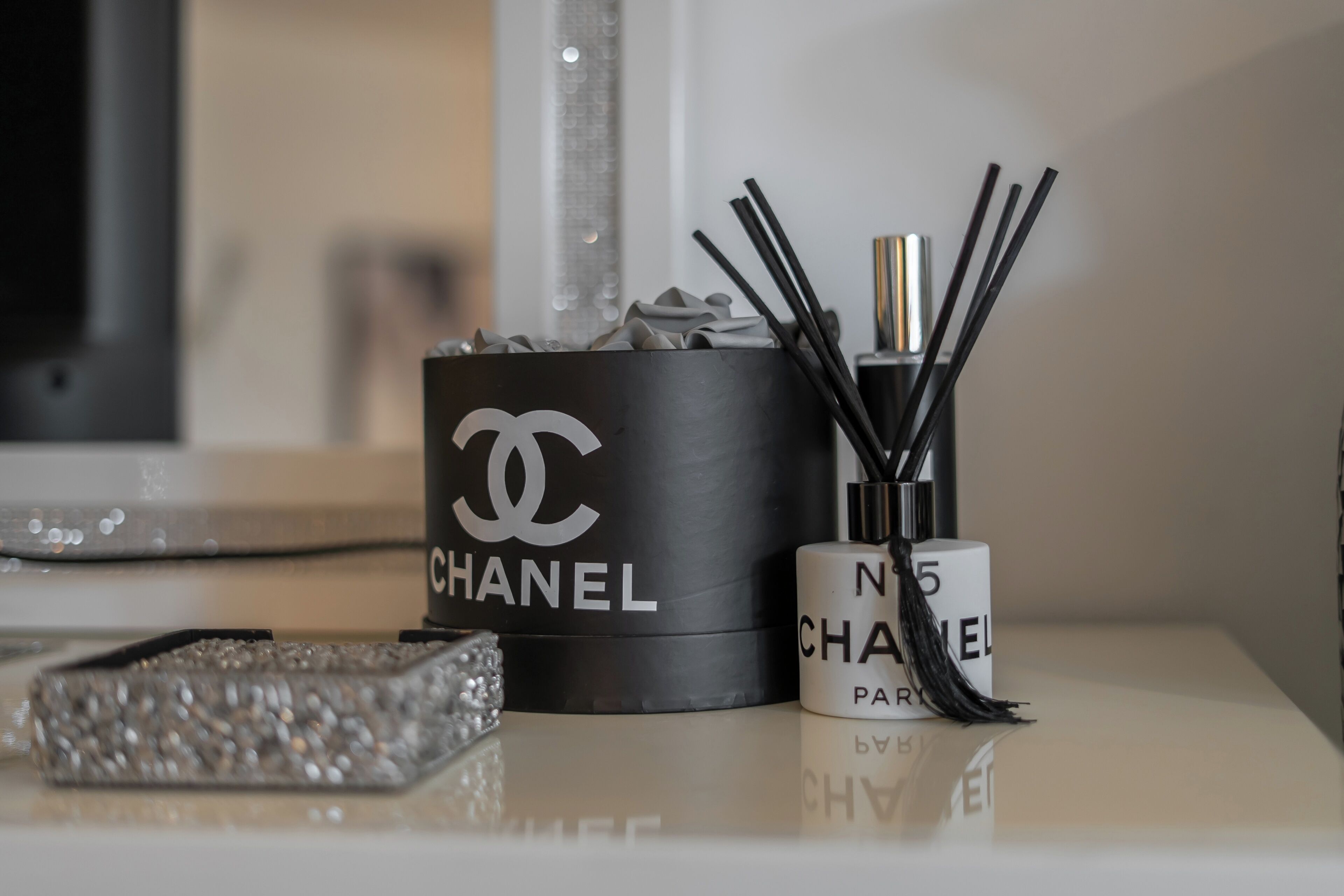 A black Chanel perfume box and a white Chanel perfume bottle on a reflective surface.