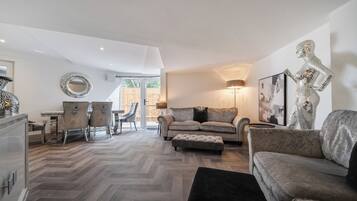 A spacious living area with a herringbone floor, a sofa set, a dining table with chairs, and a decorative mirror.