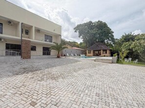 Un edificio con un patio empedrado, una pequeña construcción con techo de paja y un árbol grande.