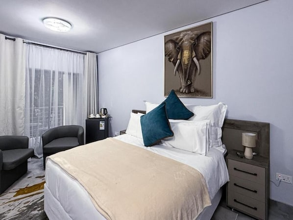 Una habitación de hotel con cama, mesita de noche, lámpara, silla y ventana con cortinas.