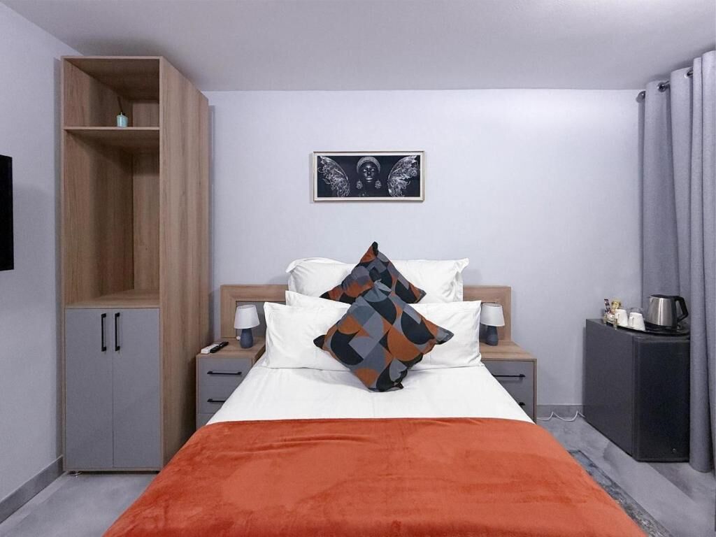 A bedroom with a bed, a nightstand, a wardrobe, a framed picture on the wall, and a side table.