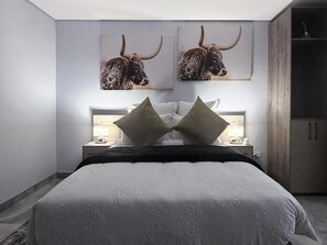 Un dormitorio con una cama grande, dos mesitas de noche con lámparas, y dos obras de arte colgadas en la pared representando toros.