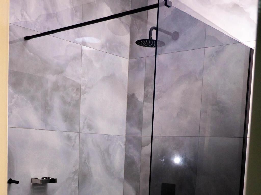 Ducha con cabezal de ducha de mano y puerta de vidrio.