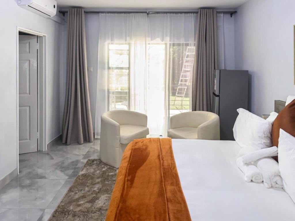 A hotel room with a bed, two chairs, a wardrobe, and a sliding glass door to the outside.