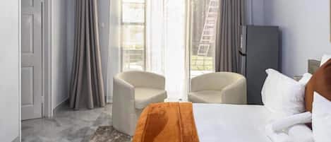 A hotel room with a bed, two chairs, a wardrobe, and a sliding glass door to the outside.