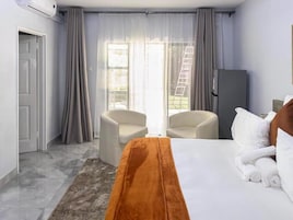Habitación de hotel con cama, dos sillas, un armario y un ventanal corredizo al exterior.