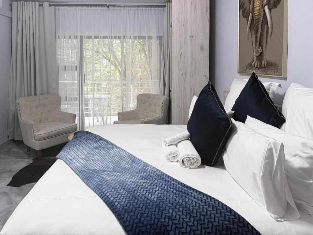 A hotel room with a large bed, two armchairs, a window with curtains, and a wall-mounted artwork.