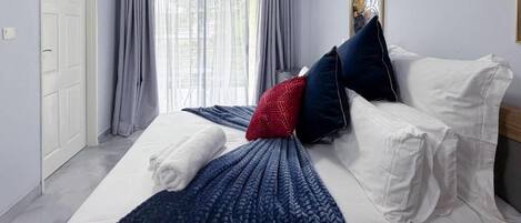 Habitación de hotel con cama, ventana con cortinas, una puerta y un aire acondicionado instalado en la pared.